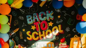 Tahvlile kirjutatud 'Back to School' tekst koos õhupallide ja koolitarvetega.
