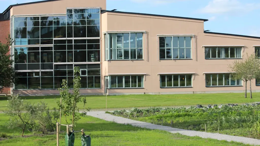 Moodne haridushoone suure klaasfassaadiga ümbritsetud rohelise muruplatsi ja noorte puudega