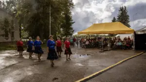 Viis naist tantsivad õues asfaldil, samal ajal kui publik jälgib neid kollase varjualuse all.